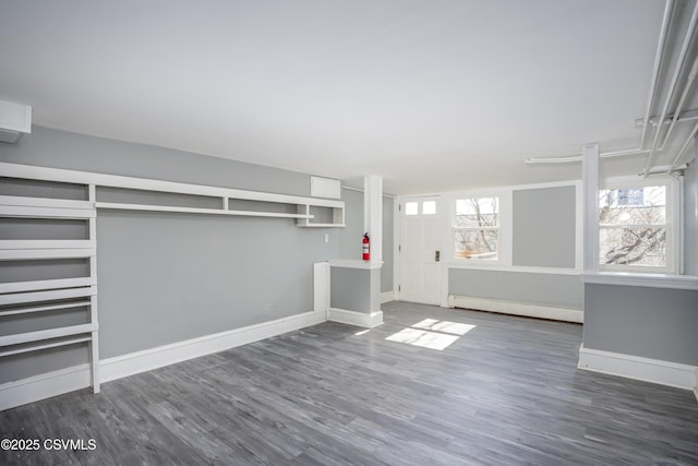 unfurnished living room featuring a baseboard heating unit, baseboards, and wood finished floors