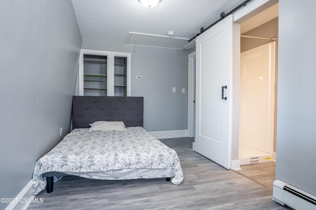 bedroom with wood finished floors, baseboards, a baseboard radiator, attic access, and a barn door