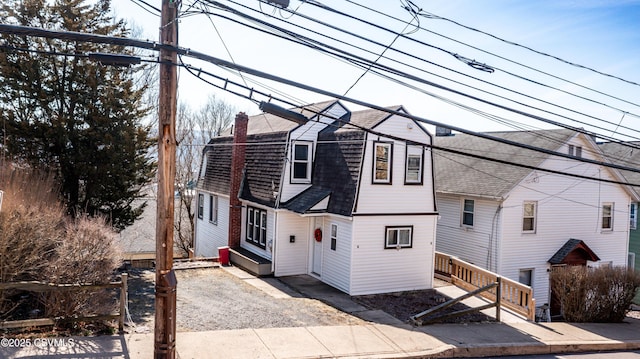 colonial inspired home with a gambrel roof, a chimney, and a shingled roof