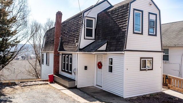 dutch colonial with entry steps, a gambrel roof, roof with shingles, and a chimney