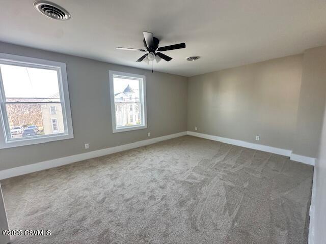 carpeted spare room with visible vents, baseboards, and ceiling fan