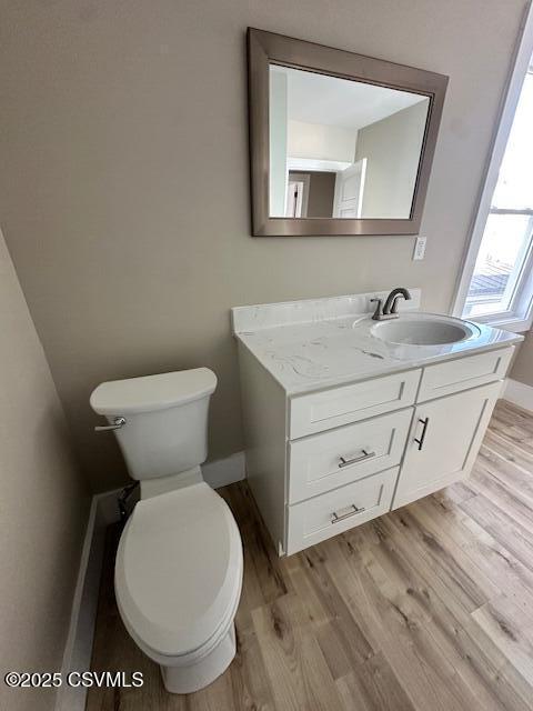 half bathroom with baseboards, toilet, wood finished floors, and vanity