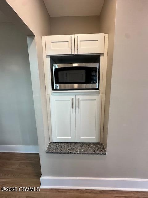 room details featuring stainless steel microwave, white cabinets, wood finished floors, and baseboards