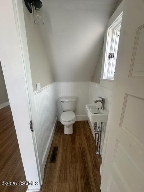 bathroom featuring wood finished floors, visible vents, lofted ceiling, wainscoting, and toilet