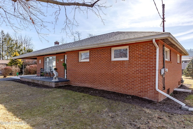 exterior space featuring brick siding, a front yard, roof with shingles, a chimney, and a patio