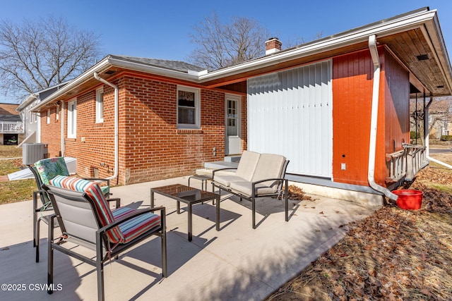 rear view of house with central AC unit, an outdoor living space, a chimney, a patio area, and brick siding