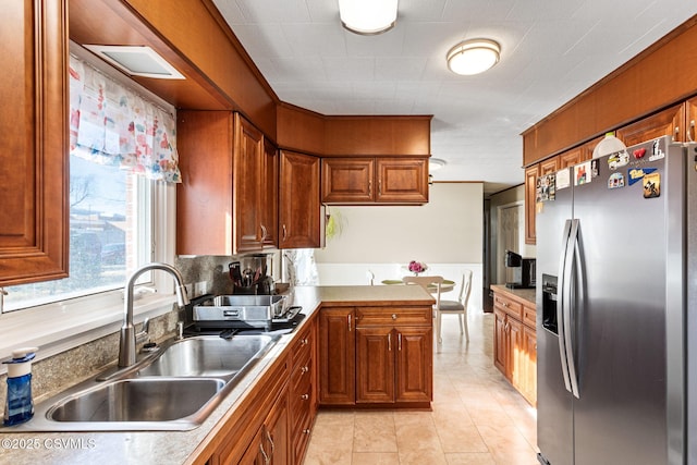 kitchen featuring brown cabinetry, a sink, a peninsula, and stainless steel fridge with ice dispenser