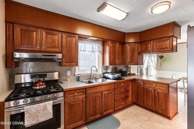 kitchen featuring brown cabinets, under cabinet range hood, a sink, gas stove, and light countertops