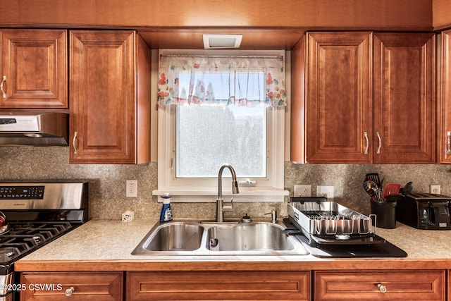 kitchen with brown cabinetry, gas stove, extractor fan, and a sink