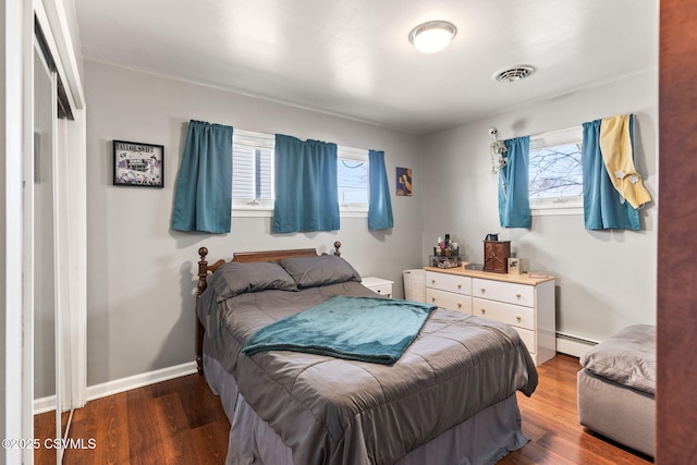 bedroom with a baseboard radiator, multiple windows, baseboards, and wood finished floors