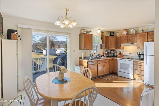 kitchen with under cabinet range hood, white appliances, a chandelier, and brown cabinetry