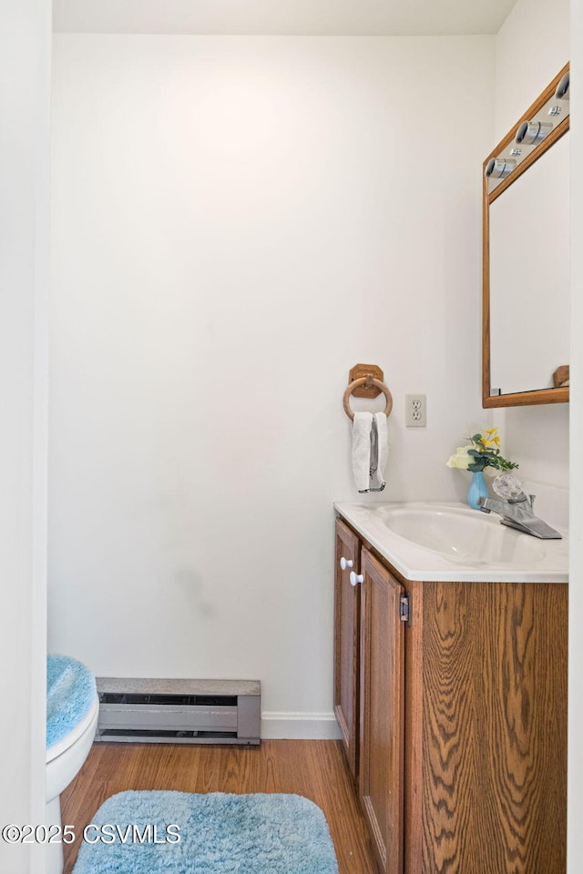 bathroom with baseboard heating, toilet, vanity, and wood finished floors