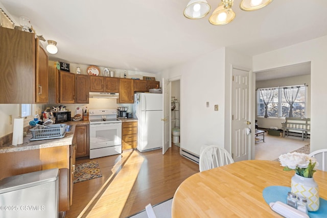 kitchen featuring light wood finished floors, under cabinet range hood, light countertops, brown cabinets, and white appliances