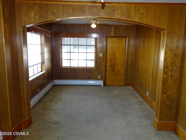 carpeted spare room with ceiling fan, wood walls, and a baseboard radiator