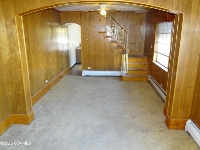 carpeted spare room featuring arched walkways, wooden walls, and a baseboard radiator