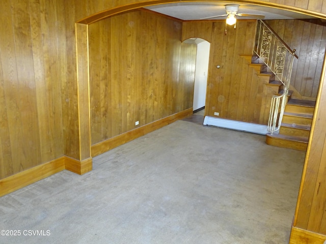 unfurnished room with a ceiling fan, arched walkways, carpet floors, wood walls, and a baseboard radiator