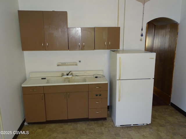 kitchen with light countertops, arched walkways, freestanding refrigerator, and a sink