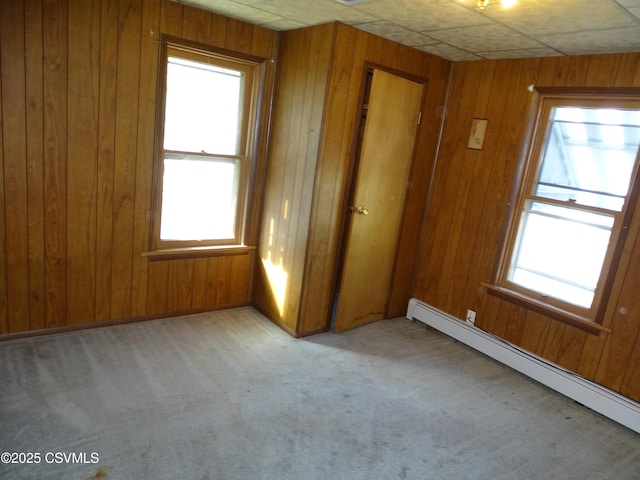 unfurnished bedroom with baseboard heating, light colored carpet, and wood walls