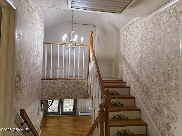 stairway featuring an inviting chandelier, baseboard heating, vaulted ceiling, and wood finished floors