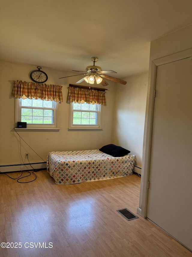bedroom featuring a ceiling fan, a baseboard heating unit, wood finished floors, and visible vents