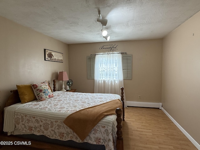 bedroom with track lighting, wood finished floors, baseboards, baseboard heating, and a textured ceiling