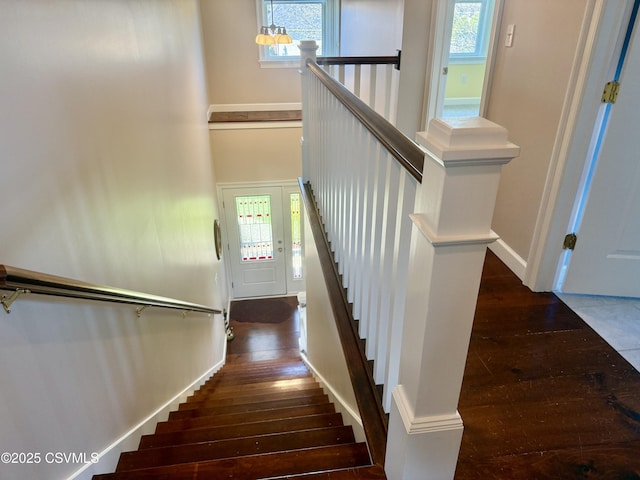 stairway featuring baseboards, plenty of natural light, and hardwood / wood-style floors