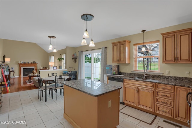 kitchen featuring vaulted ceiling, a kitchen island, stainless steel dishwasher, a sink, and hanging light fixtures