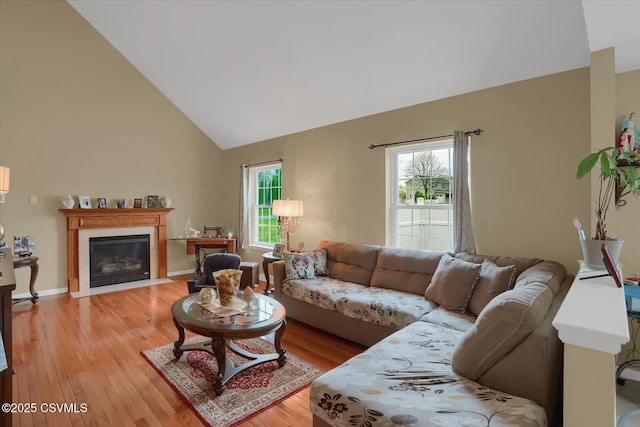 living area featuring a fireplace with flush hearth, light wood-type flooring, high vaulted ceiling, and a wealth of natural light