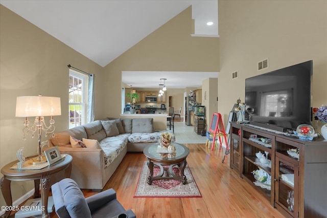 living room featuring light wood finished floors, visible vents, high vaulted ceiling, and an inviting chandelier