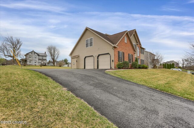 view of side of home with a lawn, brick siding, an attached garage, driveway, and a residential view
