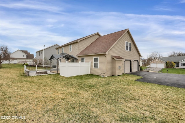 rear view of house featuring a shingled roof, an attached garage, a lawn, aphalt driveway, and fence