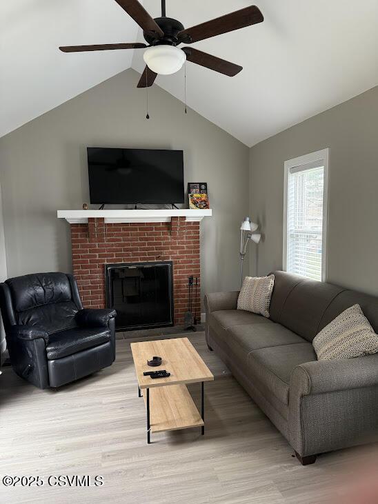 living room with a brick fireplace, ceiling fan, vaulted ceiling, and wood finished floors