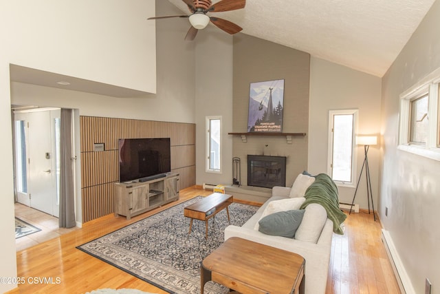 living room with a brick fireplace, a baseboard radiator, ceiling fan, hardwood / wood-style flooring, and high vaulted ceiling