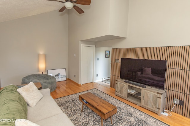 living area featuring high vaulted ceiling, a ceiling fan, baseboard heating, wood finished floors, and baseboards