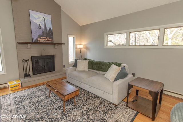 living area with a baseboard radiator, wood finished floors, a brick fireplace, and lofted ceiling