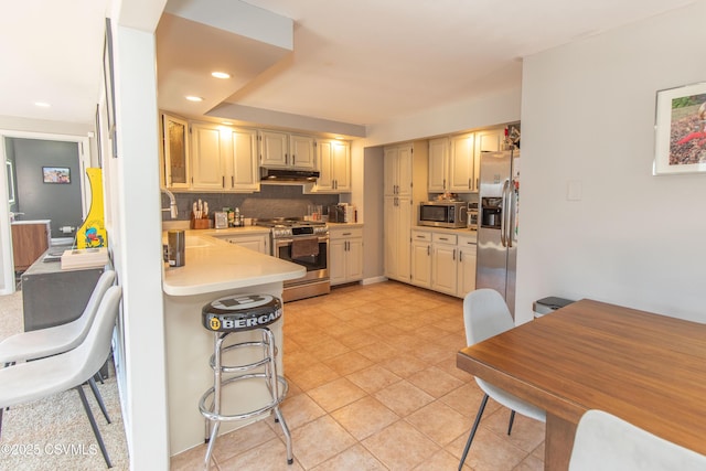 kitchen with tasteful backsplash, recessed lighting, light countertops, under cabinet range hood, and appliances with stainless steel finishes