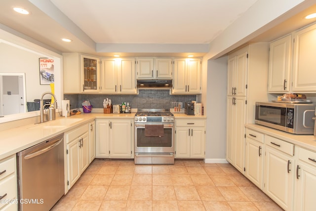 kitchen with a sink, light countertops, under cabinet range hood, stainless steel appliances, and backsplash
