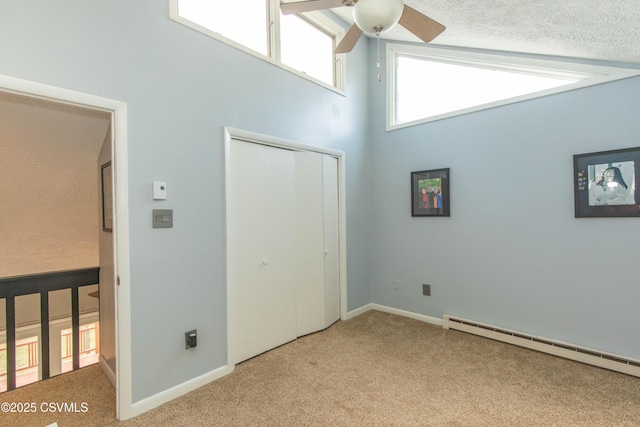 unfurnished bedroom with a closet, a high ceiling, ceiling fan, a baseboard radiator, and carpet flooring