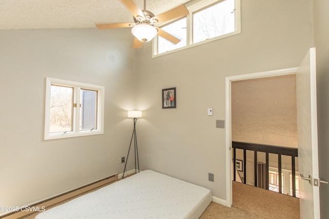 carpeted bedroom featuring a baseboard heating unit, a towering ceiling, a ceiling fan, and baseboards