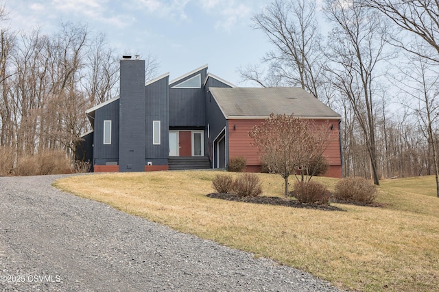 view of front of home featuring a front yard, driveway, a chimney, and an attached garage