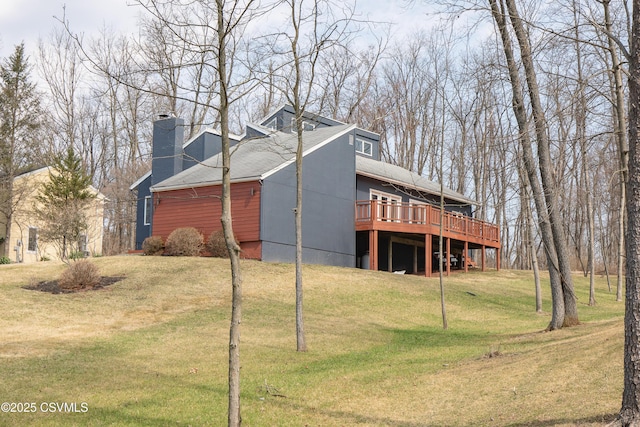 view of property exterior featuring a yard, a shingled roof, a deck, and a chimney