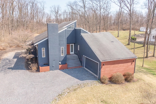 view of front of house with a front yard, a shingled roof, driveway, and a chimney