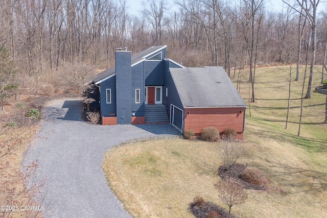 view of front of house featuring a chimney, a front lawn, and gravel driveway