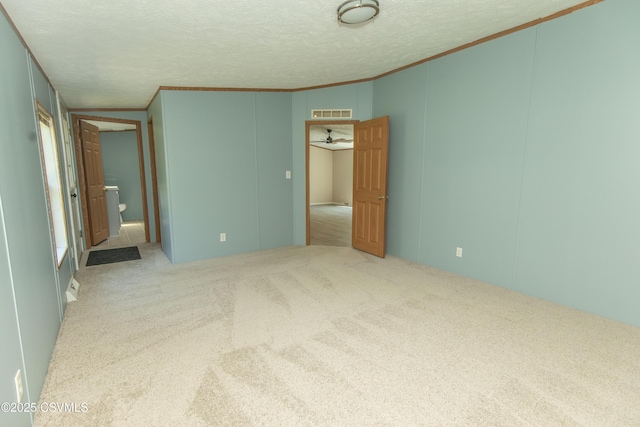 unfurnished bedroom with crown molding, carpet, a decorative wall, and a textured ceiling