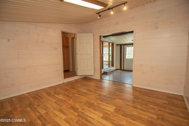 empty room with track lighting, baseboards, wood finished floors, and wooden walls