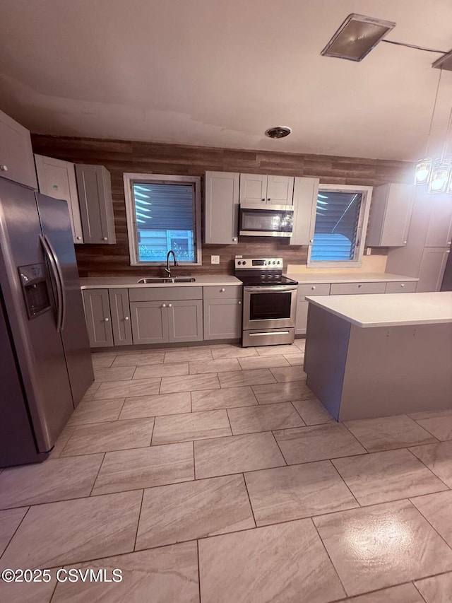 kitchen featuring gray cabinets, stainless steel appliances, light countertops, backsplash, and a sink