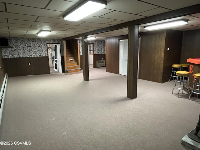 finished basement with stairway, a bar, wood walls, carpet flooring, and a paneled ceiling