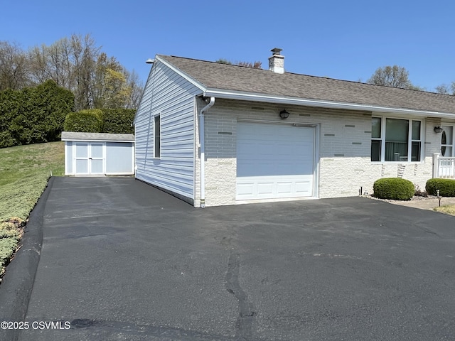 view of home's exterior featuring a shed, a chimney, aphalt driveway, an outbuilding, and a garage