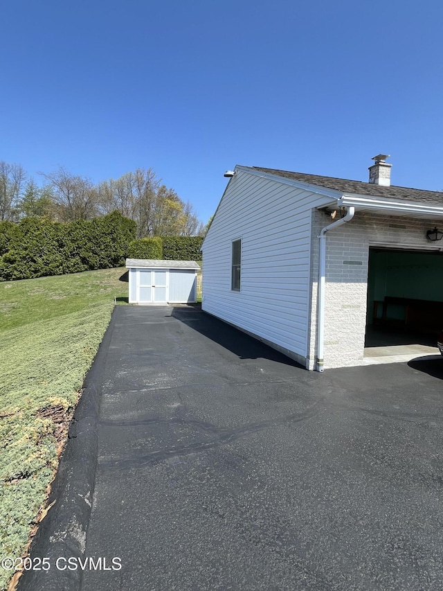 view of side of property with a chimney, a yard, a shed, an outbuilding, and brick siding