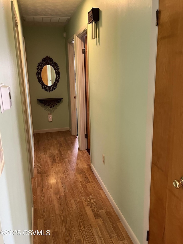 corridor featuring visible vents, baseboards, and wood finished floors